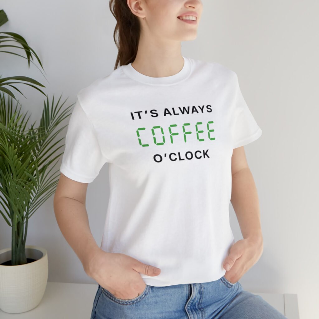A young woman wearing a white Funny T-Shirt saying "It's always coffee o'clock" in letters looking like digits on a digital clock.