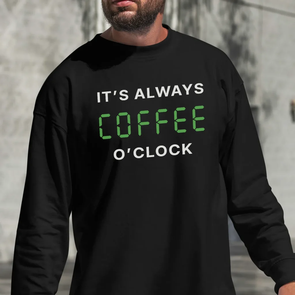 A man outside wearing a black Sweatshirt saying "It's always coffee o'clock" in letters looking like digits on a digital clock.