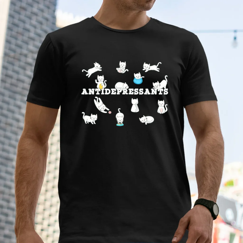 A man outside wearing a black funny T-Shirt for cat lovers with cartoony pictures of funny cats saying "Antidepressants".