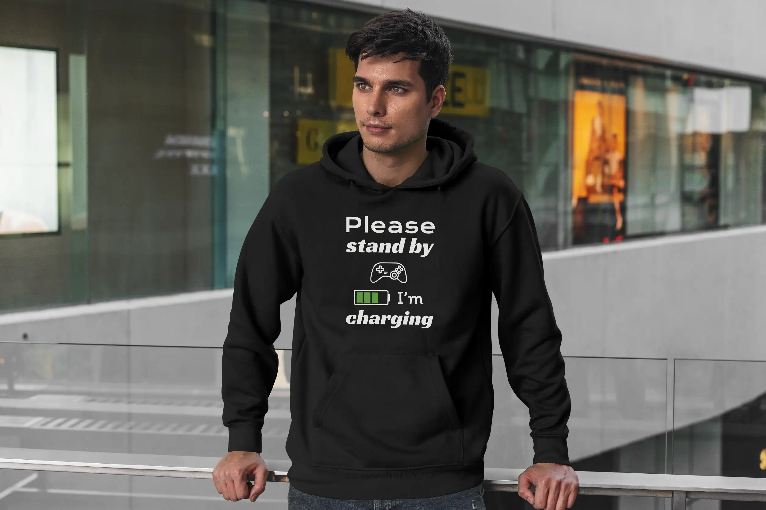 A handsome man outside wearing a black Funny Hoodie for Gamers featuring a picture of a gamepad and saying "Please stand by, I'm charging".