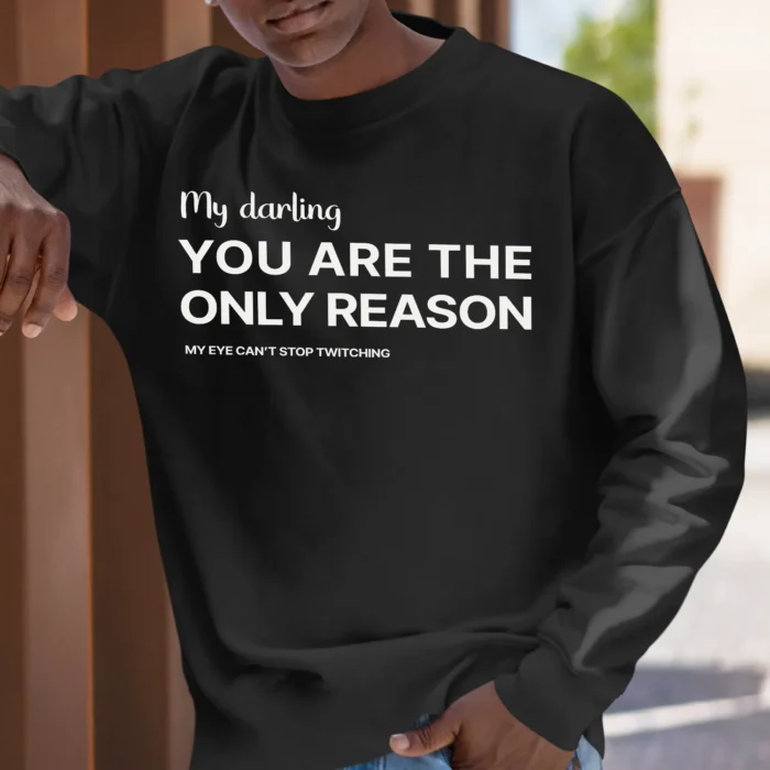 A young man outside wearing a funny sweatshirt saying "My darling, you’re the only reason… My eye can’t stop twitching", black color