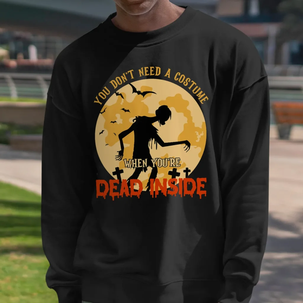 A young african-american man outside wearing a funny Halloween Sweatshirt with a zombie print saying "You don't need a costume when you're dead inside". Black color