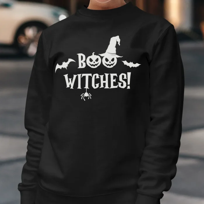 A young woman outside wearing a funny Halloween Sweatshirt with a witch's hat saying "Boo Witches!" Black color