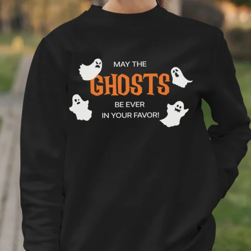 A young woman outside wearing a funny Halloween Sweatshirt with ghosts saying "May the ghosts be ever in your favor!" Black color