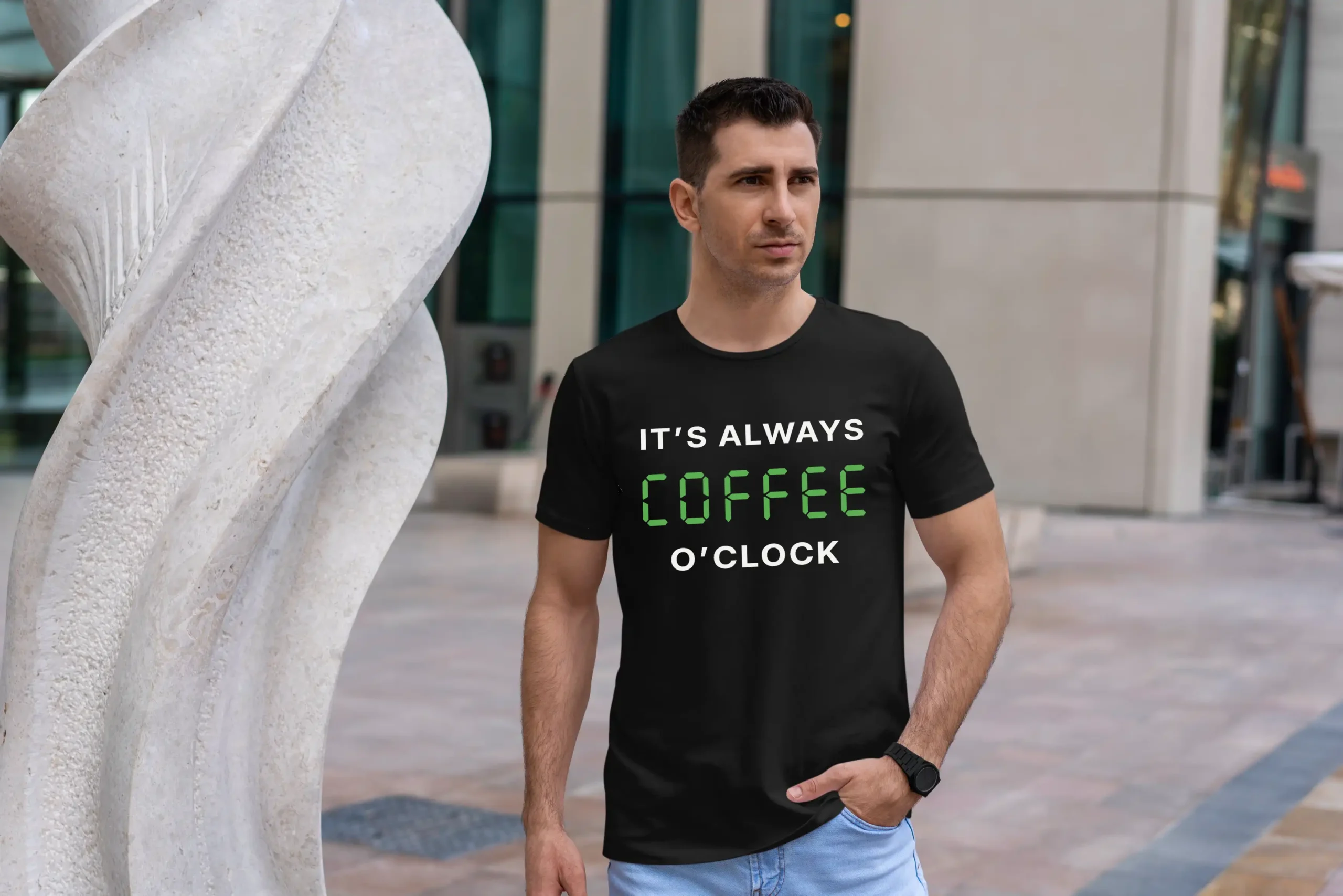 A man outside wearing a black T-Shirt saying "It's always coffee o'clock" in letters looking like digits on a digital clock.